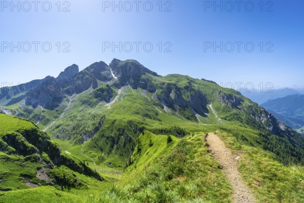 Scenic view of a hiking path leading through vibrant green mountains under a clear blue sky in the italian dolomites