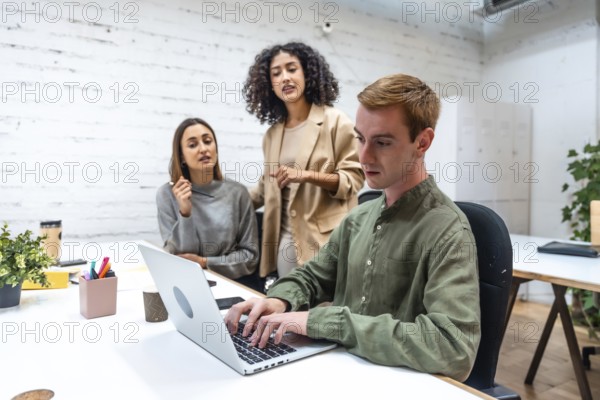 Three diverse colleagues discussing work issues and using laptop in a coworking space