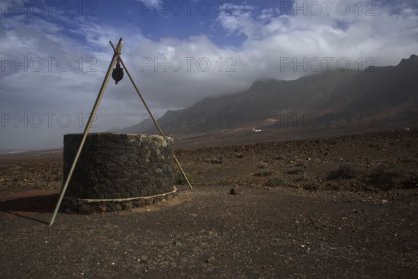 Stone fountain in lonely, barren volcanic landscape near Cofete in front of cloudy mountains, Pajara, Fuerteventura, Canary Islands, Spain, Europe