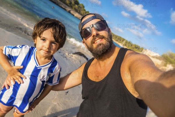 A man and a boy are posing for a picture on a beach. The boy is wearing a blue and white striped shirt