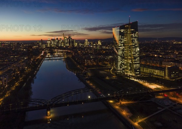 The lights in the offices of the European Central Bank (ECB) and in the skyscrapers of Frankfurt's banking skyline glow in the evening shortly after sunset. (Aerial view with a drone), Frankfurt am Main, Osthafen, Hesse, Germany, Europe
