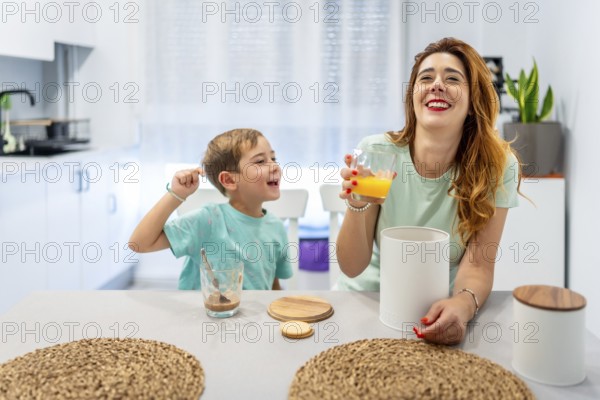 Mother and boy laughing while eating breakfast before going to school at home