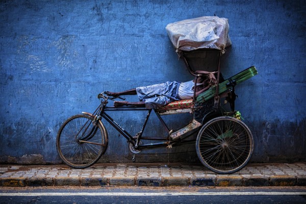 DELHI, INDIA, SEPTEMBER 11, 2011: Indian cycle rickshaw driver sleeping on his bicycle in the street of New Delhi, India. Cycle rickshaws were used in Kolkata starting about 1930 and are now common in rural and urban areas of India