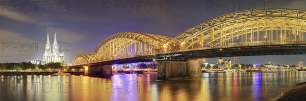Panorama of the illuminated Cologne Cathedral with Hohenzoller Bridge at night, with reflection of the lights in the Rhine, Cologne, North Rhine-Westphalia, Germany, Europe