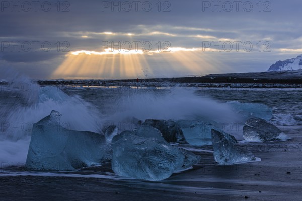 Waves breaking on icebergs on the black beach of Breidamerkursandur, sunset, near Jökullsarlon, Sudurland, Iceland, Europe