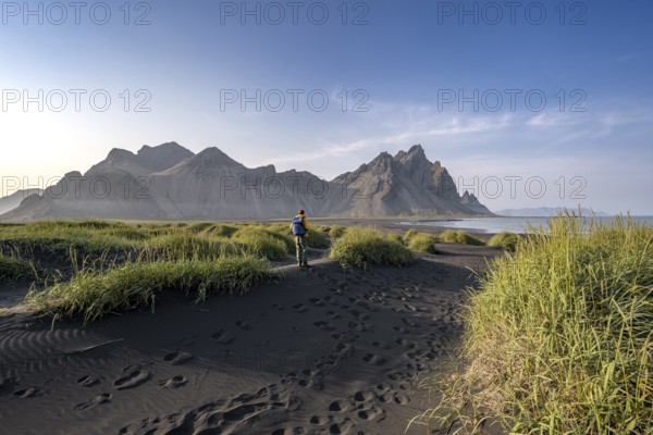 Tourist on a sand dune, Black beach with volcanic sand, Sand beach, Dunes with grass, Stokksnes headland, Klifatindur mountain range, Austurland, East Iceland, Iceland, Europe