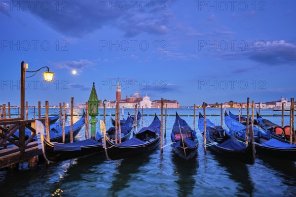 Romantic vacation Venice travel background, gondolas at Saint Mark (San Marco) square and Basilica San Giorgio Maggiore Church seen across Venice lagoon with full moon. Venice, Italy, Europe