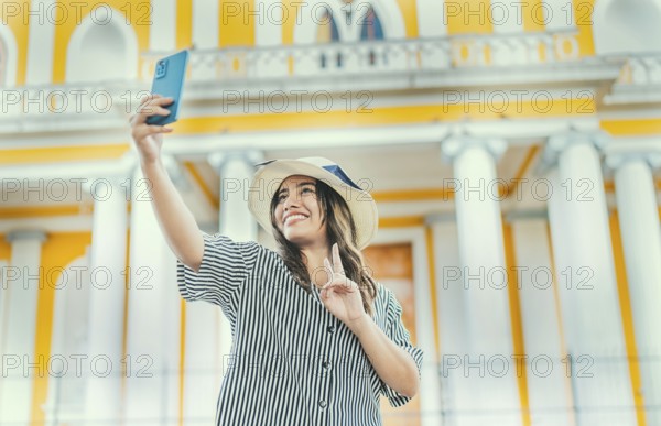 Young tourist woman with hat taking selfie in a square. Selfies and vacation concept. Beautiful tourist girl taking selfie in the cathedral of Granada