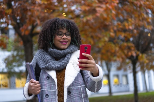 Portrait of black ethnic girl walking in college college in autumn talking on phone back to school