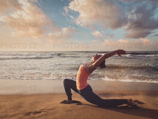 Vintage retro effect filtered hipster style image of Yoga outdoors, sporty fit woman practices yoga Anjaneyasana, low crescent lunge pose outdoors at beach on sunset