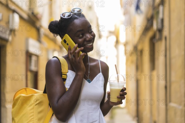 Young african woman talking with the mobile and drinking milkshake stranding on the street
