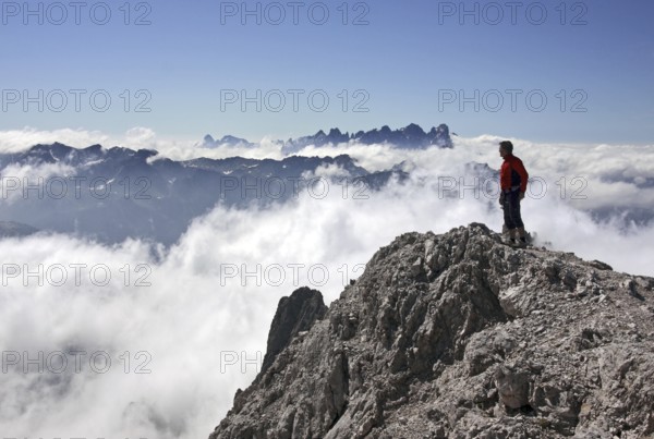 Mountaineer looking from the Cima Scalieret over blanket of clouds and mountain peaks of the Italian Dolomites, Dolomiti di Pala, Catenaccio, Val di Fassa, Italy, Europe