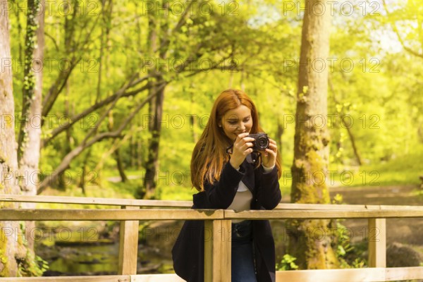 Woman photographer with a black jacket enjoying in an autumn park, taking pictures on a wooden bridge