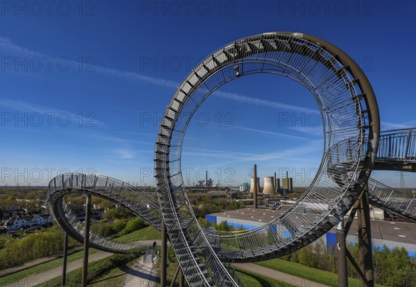 Duisburg, Ruhr area, North Rhine-Westphalia, Germany - Industrial landscape in the Ruhr area, Tiger & Turtle - Magic Mountain in front of HKM steelworks. Tiger and Turtle - Magic Mountain is a large sculpture modelled on a rollercoaster on Heinrich-Hildebrand-Höhe in Angerpark in Duisburg-Angerhausen. The large sculpture is a work of art by Heike Mutter and Ulrich Genth, which was developed as part of the Ruhr.2010 Capital of Culture programme. HKM steelworks, with blast furnaces, Duisburg-Huckingen gas-fired power station on the Rhine. HKM Hüttenwerk Krupp Mannesmann in Duisburg-Hüttenheim. Current shareholdings: 50 % thyssenkrupp Steel Europe AG, 30 % Salzgitter Mannesmann GmbH, 20 % Vallourec Tubes S.A.S. Steel manufacturer Thyssen-Krupp Steel decides to separate from HKM