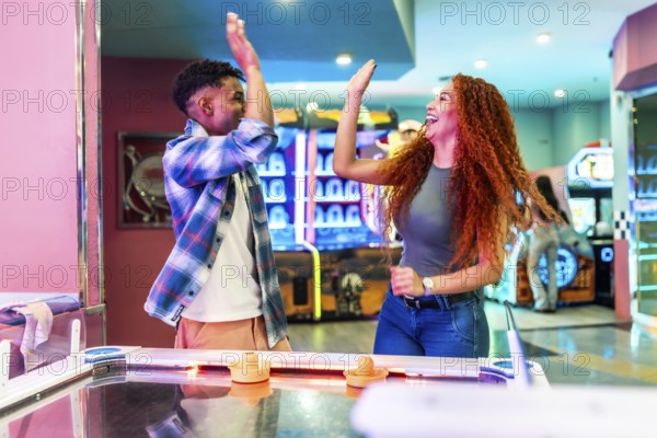 Two friends giving high five while enjoying a game of air hockey in a vibrant entertainment center, celebrating a point or victory