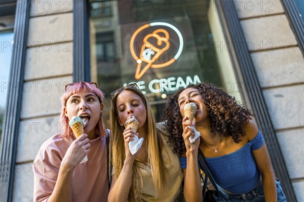 Low angle view photo of three diverse female friends enjoying eating a delicious ice cream outside the store