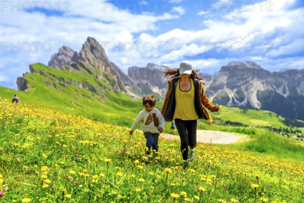 Mother and son running through a field of wildflowers in the italian dolomites mountains, enjoying summer vacation in the seceda region