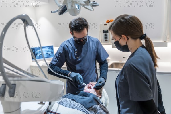 Dentist wearing magnifying glasses and face mask performing a dental procedure on a senior female patient assisted by a dental nurse