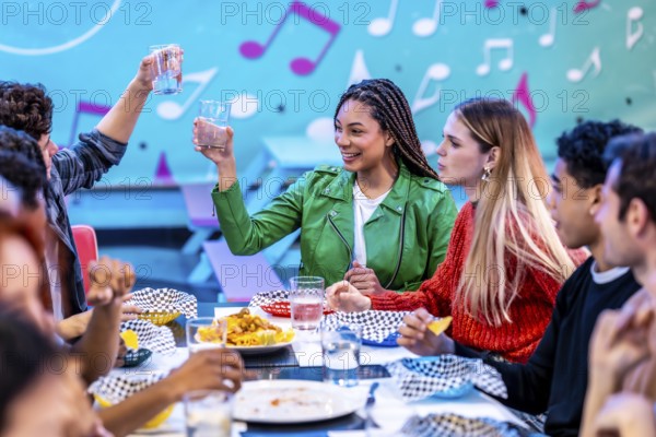 Multiethnic friends enjoying a meal and drinks at a bowling alley restaurant, celebrating their weekend together