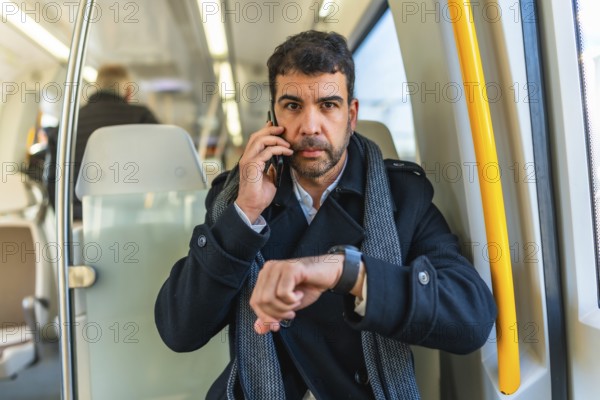 Frontal portrait of a serious caucasian adult, businessman using smartwatch while talking to the mobile at metro