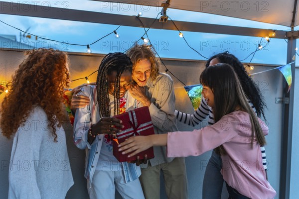 Happy millennial multi-ethnic friends celebrating birthday party in an urban rooftop at dusk