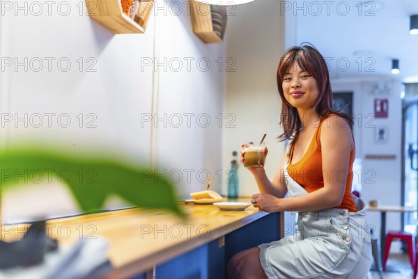 Portrait with copy space of a smiling asian youthful woman drinking coffee in a cafeteria