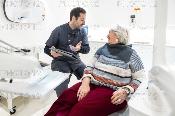 Dentist is explaining something on a tablet to a senior female patient during a consultation in a modern dental clinic