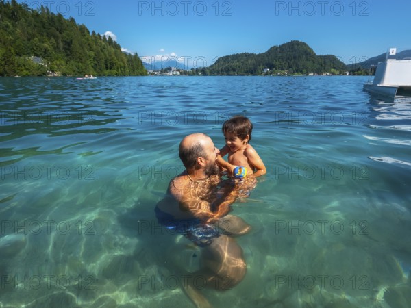 Father and son having fun swimming in the clear waters of lake bled, surrounded by the beauty of the julian alps in slovenia