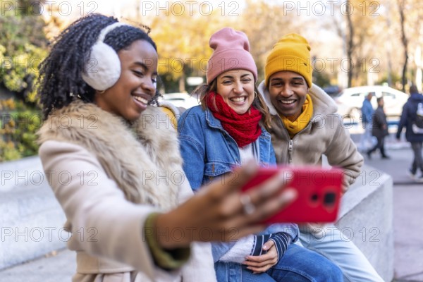Three happy multi ethnic friends enjoying the outdoors, taking a cheerful selfie in a winter city filled with laughter and warmth
