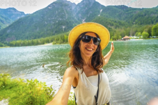 Happy tourist taking a selfie with outstretched arms at lake dobbiaco in the italian dolomites, enjoying summer holidays