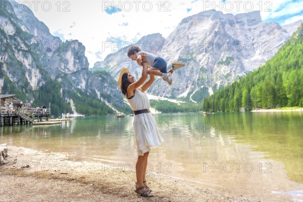 Tourist mother lifting her son in the air while enjoying summer holidays at lake braies, also called pragser wildsee, in the dolomites of italy