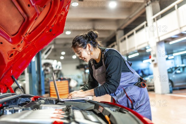 Young woman mechanic using a laptop while examining a car engine in a professional workshop
