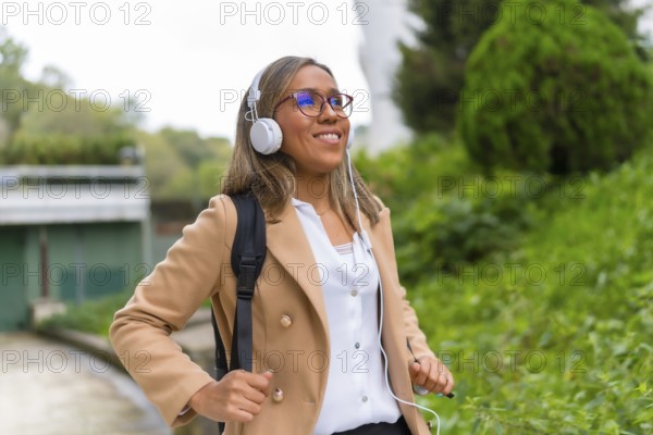 Portrait of a happy latin businesswoman listening to music commuting in the city walking down a residential area