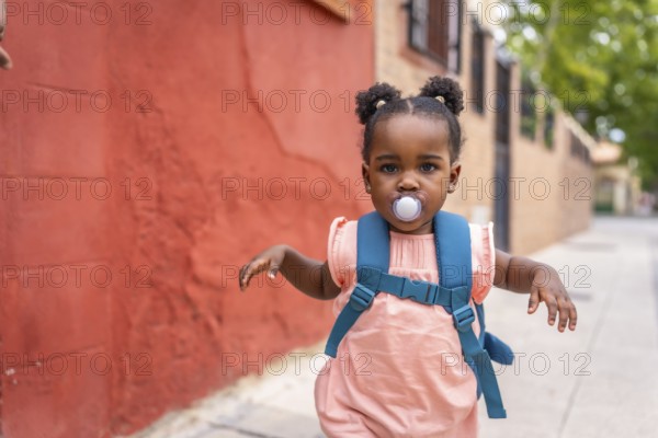 Cute baby african girl running along a street using pacifier