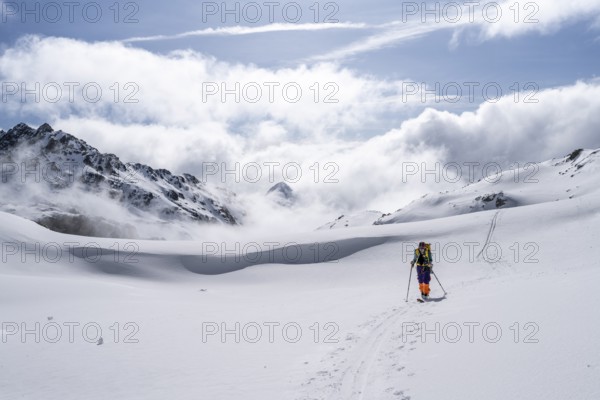 Atmospheric clouds in a wintry mountain landscape, ski tourer on the ascent to Porta d'Es-cha, Bündner Haute Route ski tour, Albula Alps, Rhaetian Alps, Grisons, Eastern Switzerland, Switzerland, Europe