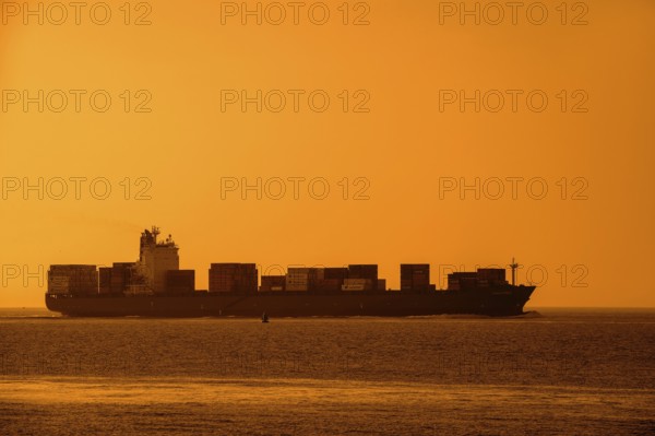 Container ship, containership Amalthea, loaded with containers silhouetted against orange sunset sky
