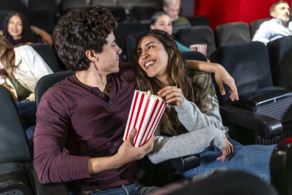 Happy couple sharing popcorn and enjoying a movie at the cinema, embracing during a romantic date