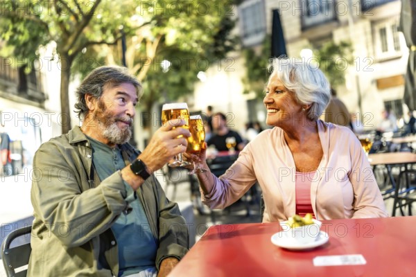 Happy relaxed senior couple toasting with beer in sidewalk cafeteria at night