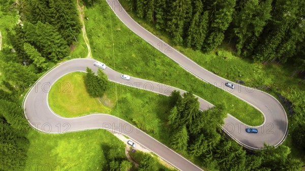 Aerial view of cars driving on a winding mountain road surrounded by lush green forest in the dolomites, italy, during summer