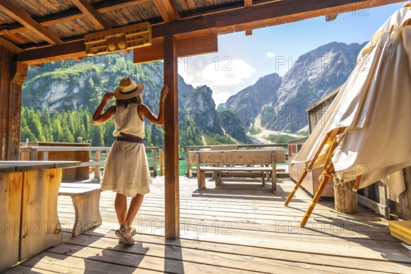 Woman wearing straw hat standing on wooden pier, admiring stunning landscape of lake braies and surrounding mountains in dolomites