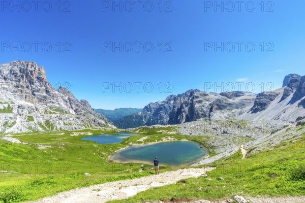 Breathtaking view of the tre cime di lavaredo and the surrounding lakes with a tourist enjoying the sunny summer day in the dolomites. Laghi dei Piani