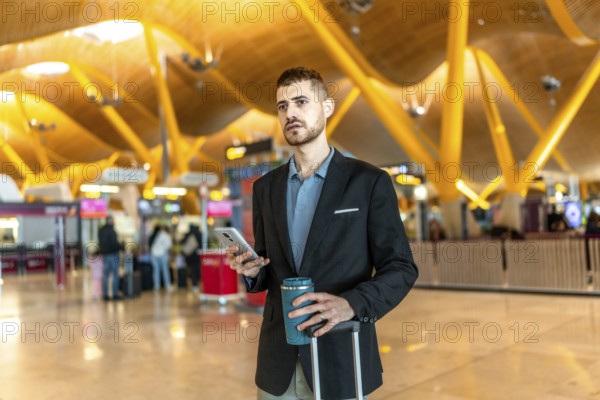 Businessman holding a reusable coffee cup and smartphone while waiting for his flight at the airport
