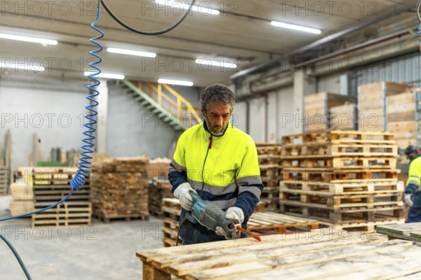 Adult caucasian man worker repairing broken pallets in a recycling plant workshop using compressed air gun machine
