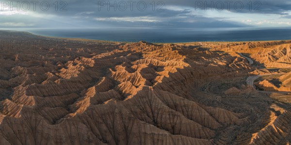 Riverbed runs through a landscape of eroded hills, badlands at sunset, Issyk Kul Lake in the background, aerial view, Canyon of the Forgotten Rivers, Issyk Kul, Kyrgyzstan, Asia