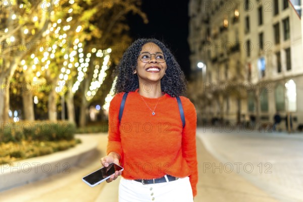 Young woman enjoying an evening stroll through a vibrant, illuminated city, engaging with her smartphone while soaking in the urban atmosphere
