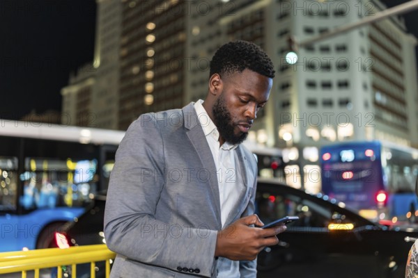 Young businessman using smartphone on a city street at night, with blurred traffic and buildings in background