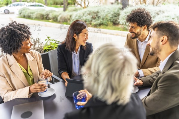 Multi-ethnic business people drinking coffee working with digital tablet sitting relaxed in a cafeteria