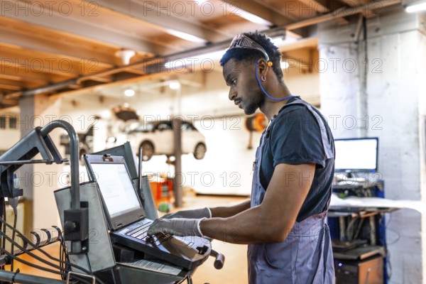 Young mechanic working diligently on a laptop for car diagnostics in a modern, well organized auto repair shop