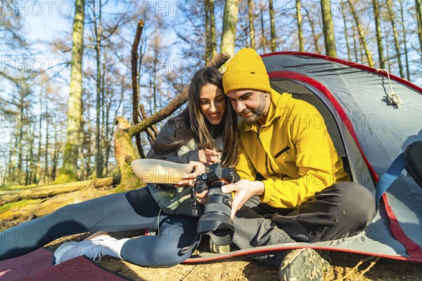 Couple of hikers reviewing photos on their camera while having a meal in front of their tent during a camping trip in the woods