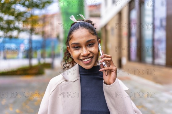 Happy african elegant woman talking to the mobile phone standing in the city street